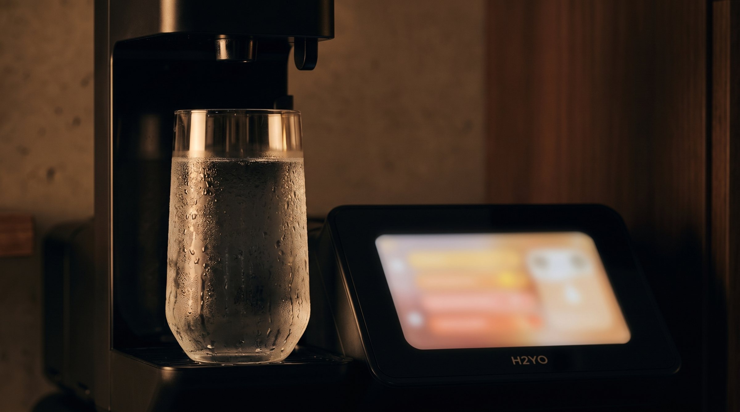 Close-up of the tap plate: a glass of chilled water under the tap, the screen blurred on the right